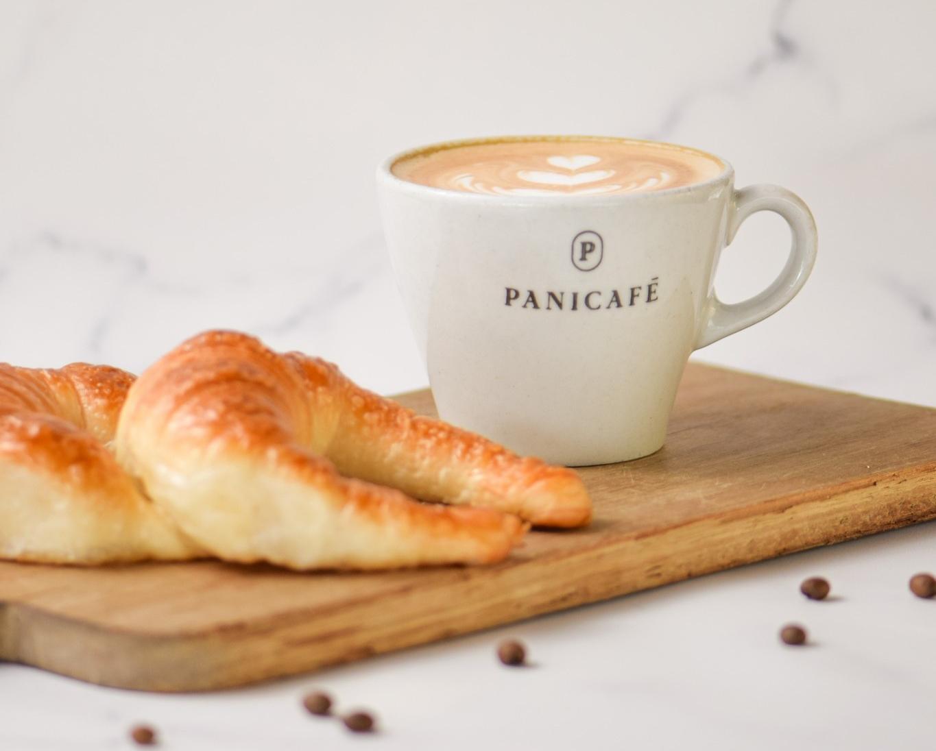 Taza de café Panicafé con medialunas sobre una tabla de madera